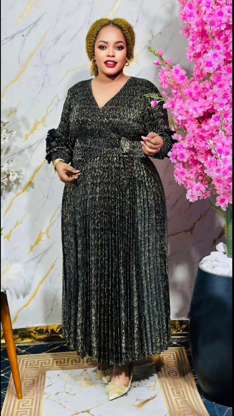 Woman in a black patterned dress holding pink flowers against a marble wall.